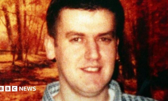 Robert Hamill with brown hair and a checked shirt smiling at the camera.