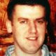 Robert Hamill with brown hair and a checked shirt smiling at the camera.