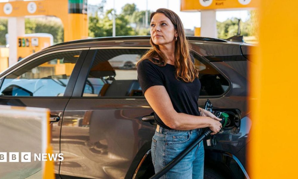 Stock photo shows a woman filling up her car with petrol at a station with yellow pumps