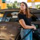 Stock photo shows a woman filling up her car with petrol at a station with yellow pumps