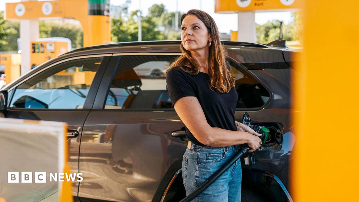 Stock photo shows a woman filling up her car with petrol at a station with yellow pumps