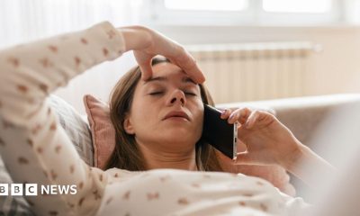 Woman lying back on a sofa with one hand on her forehead and the other hand holding a mobile phone to her ear