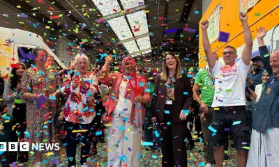 A group of people stand in a row and cheer as colourful confetti falls around them.