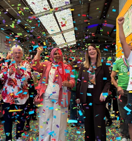 A group of people stand in a row and cheer as colourful confetti falls around them.