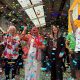 A group of people stand in a row and cheer as colourful confetti falls around them.
