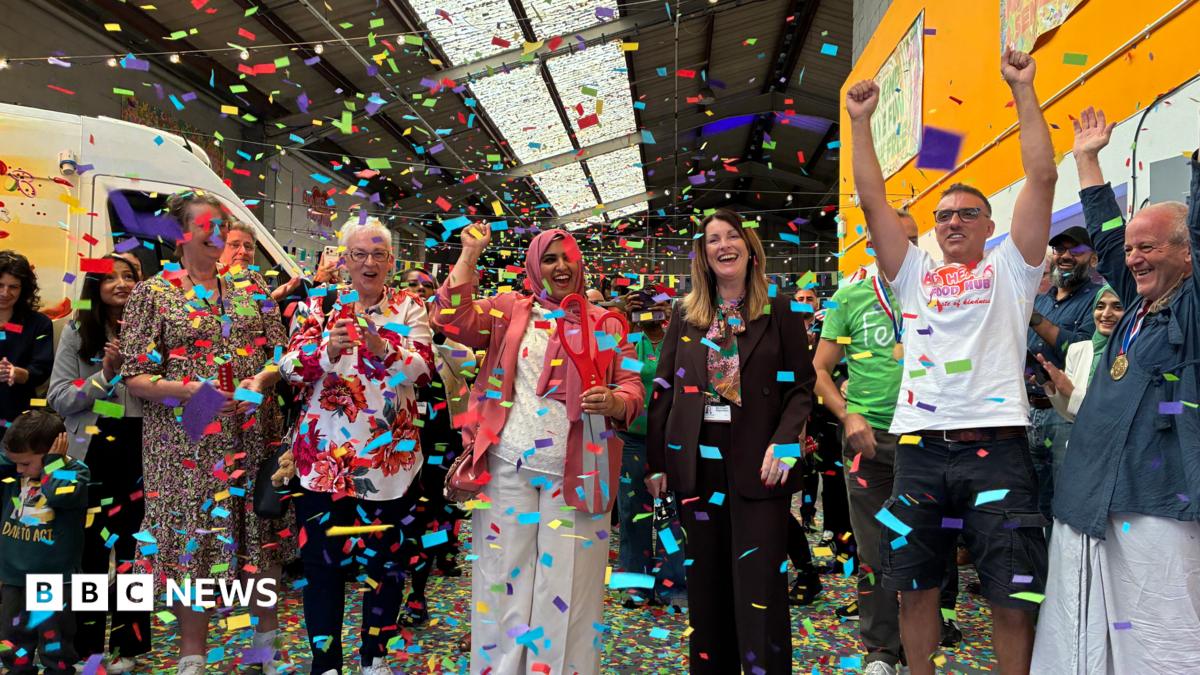 A group of people stand in a row and cheer as colourful confetti falls around them.