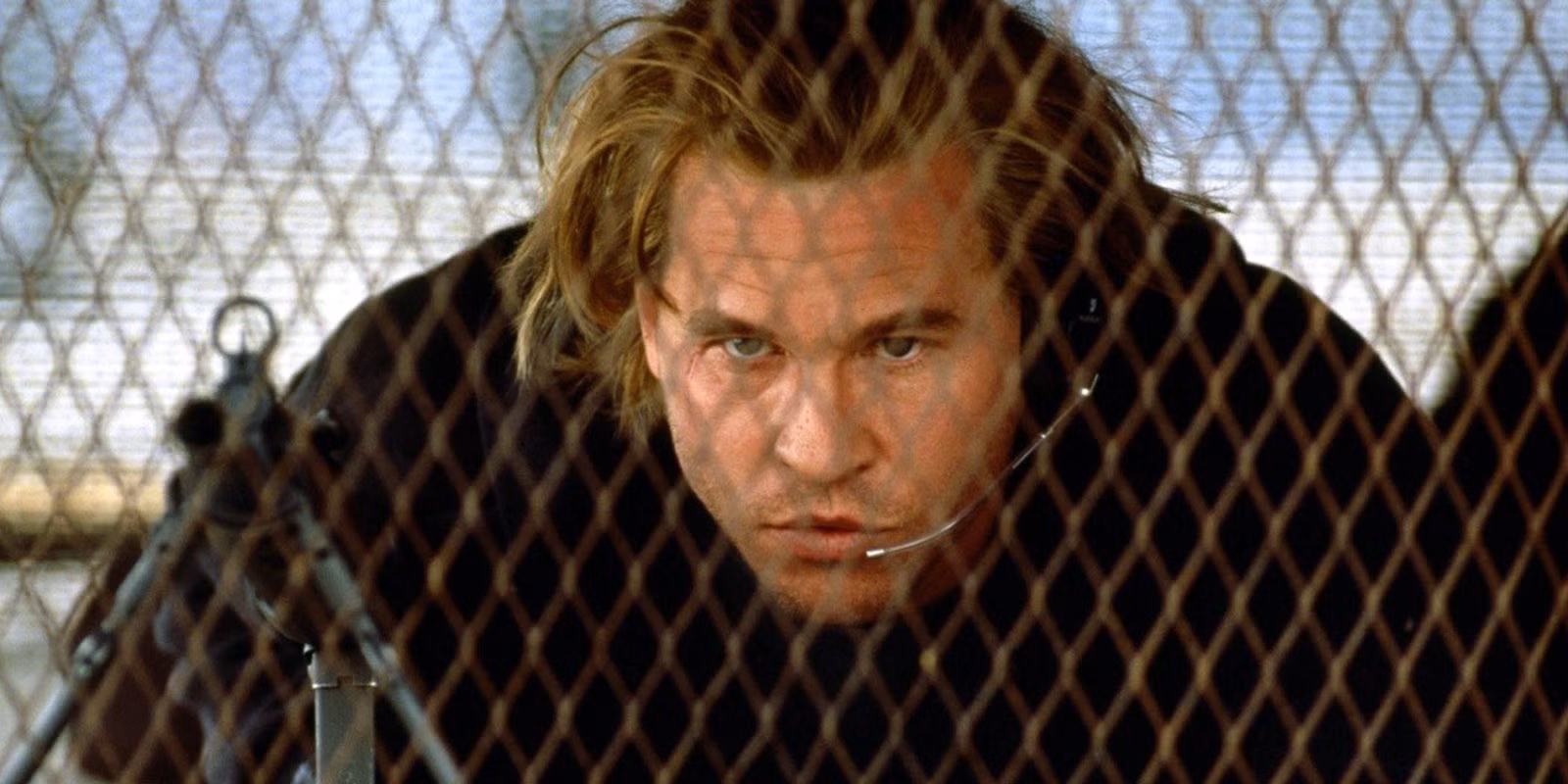 Val Kilmer behind a fence ready to aim a weapon in Heat