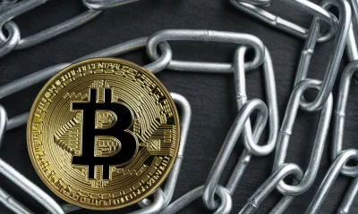 Physical Bitcoin gold coin on a convoluted shiny metal chain.
