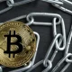Physical Bitcoin gold coin on a convoluted shiny metal chain.