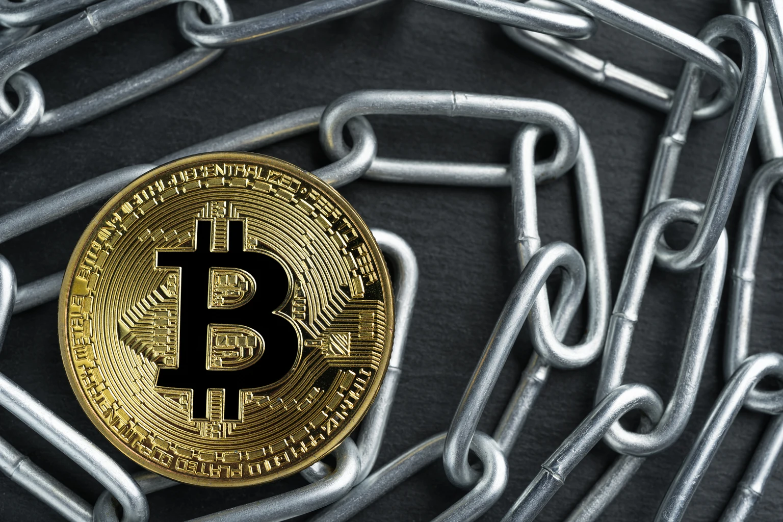Physical Bitcoin gold coin on a convoluted shiny metal chain.