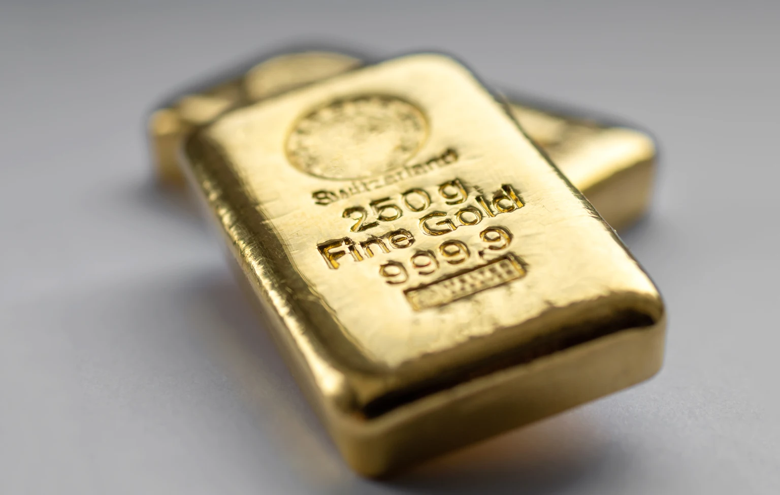 Two gold bullions weighing 250 grams each on a grey background.