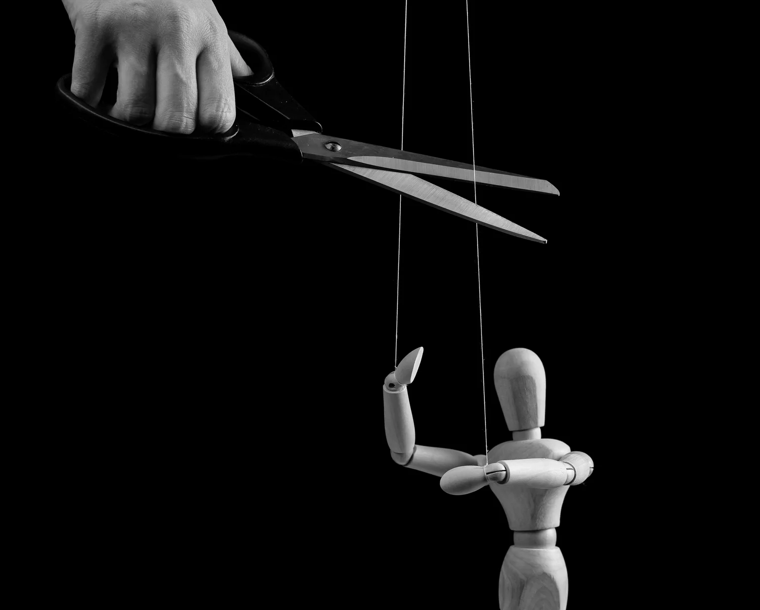Hand cutting strings over puppet with scissors. Manipulation, negative influence, control stop concept. Overcoming addiction. Black and white