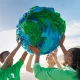 Group of young climate activists holding up a globe together by the sea