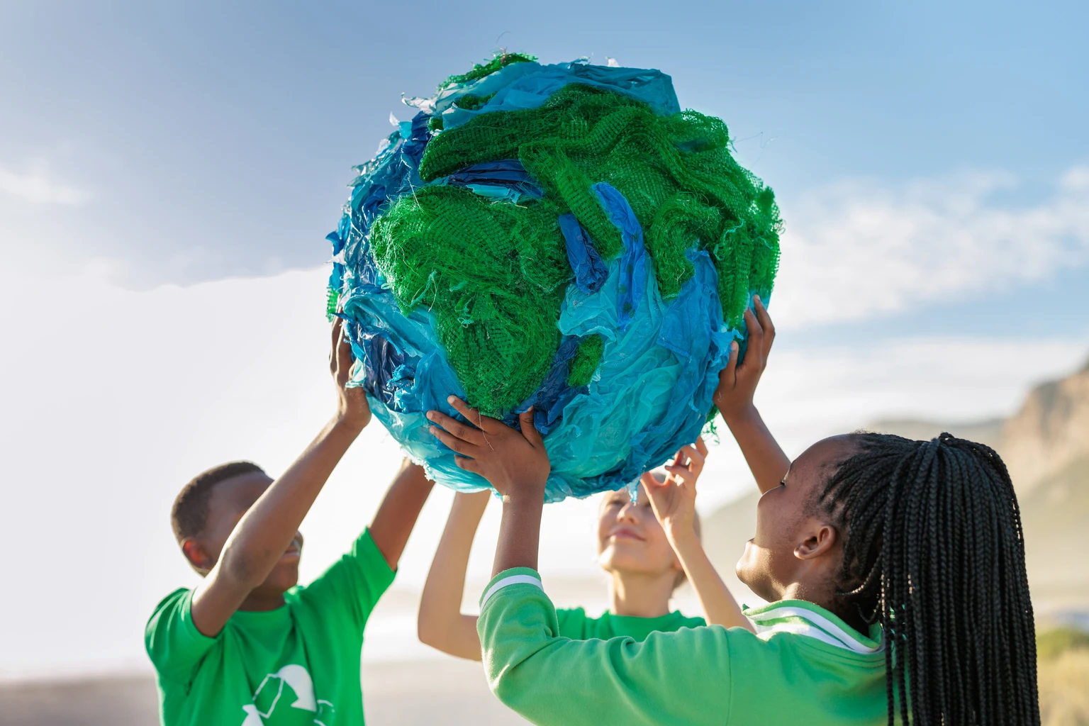 Group of young climate activists holding up a globe together by the sea