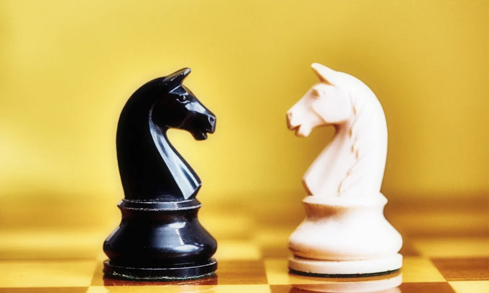 Conflict and rivalry: black and white chess knights face off against each other