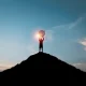 Silhouette of man holding dartboard with arrow on the top of mountain and blue sky for business achievement objective target and goal concept.