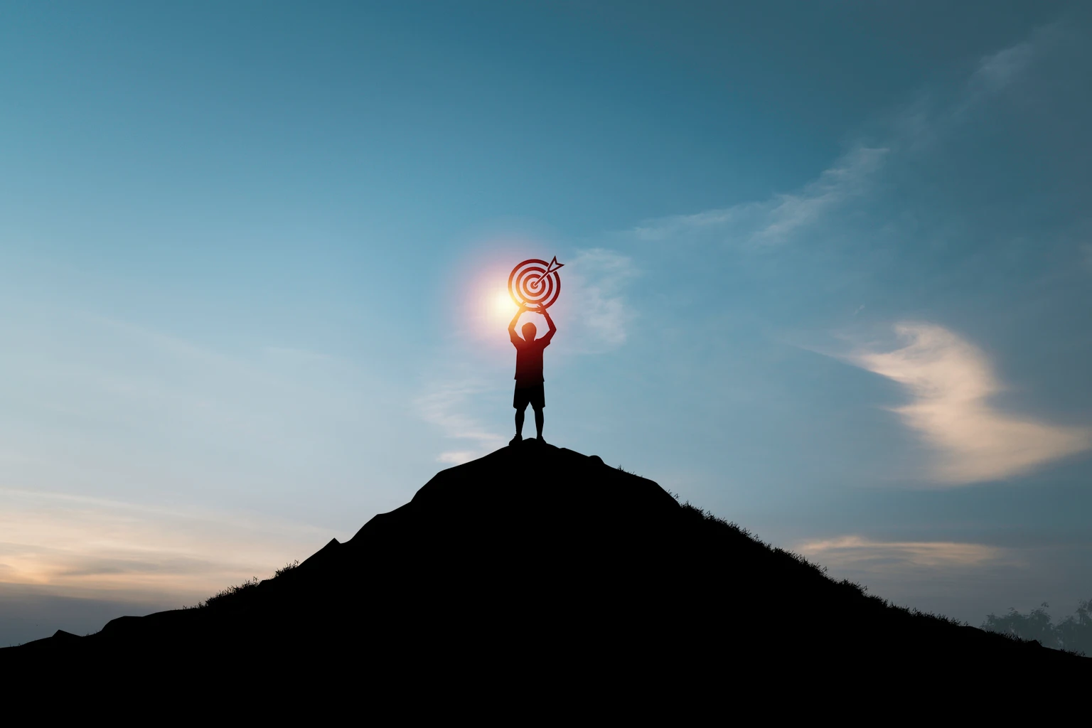 Silhouette of man holding dartboard with arrow on the top of mountain and blue sky for business achievement objective target and goal concept.