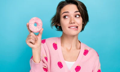 Close up photo of young lady wear pink trendy jumper strawberry print bite lips wish try eat hungry donut isolated on blue color background