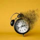 A black alarm clock dissolving on yellow background. Concept of importance of moments conveying time running out.