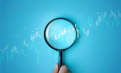Hand holding magnifying glass analyzing digital financial stock chart. Data analysis, investment research, trading strategy, and financial market concept on blue background. business stock market.