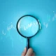 Hand holding magnifying glass analyzing digital financial stock chart. Data analysis, investment research, trading strategy, and financial market concept on blue background. business stock market.