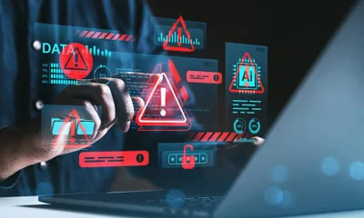 Cybersecurity threat warning concept with holographic red alert symbols over hands using laptop in dark environment, illustrating data protection risks.