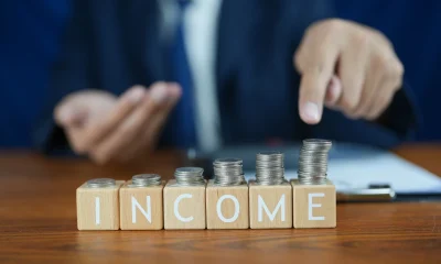 Businessman Presenting Income Growth with Stacked Coins on Wooden Table and Focused Gesture in Office Environment