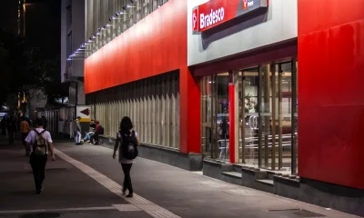 Night view of a Bradesco bank branch facade on Avenida Paulista. Pedestrians walk on the illuminated tactile sidewalk in the main financial district.