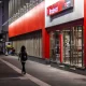 Night view of a Bradesco bank branch facade on Avenida Paulista. Pedestrians walk on the illuminated tactile sidewalk in the main financial district.