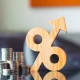 Wooden percentage symbol with upward arrow next to growing coin stacks. Financial interest rate hike, rising inflation, profitable return, and tax growth concept.
