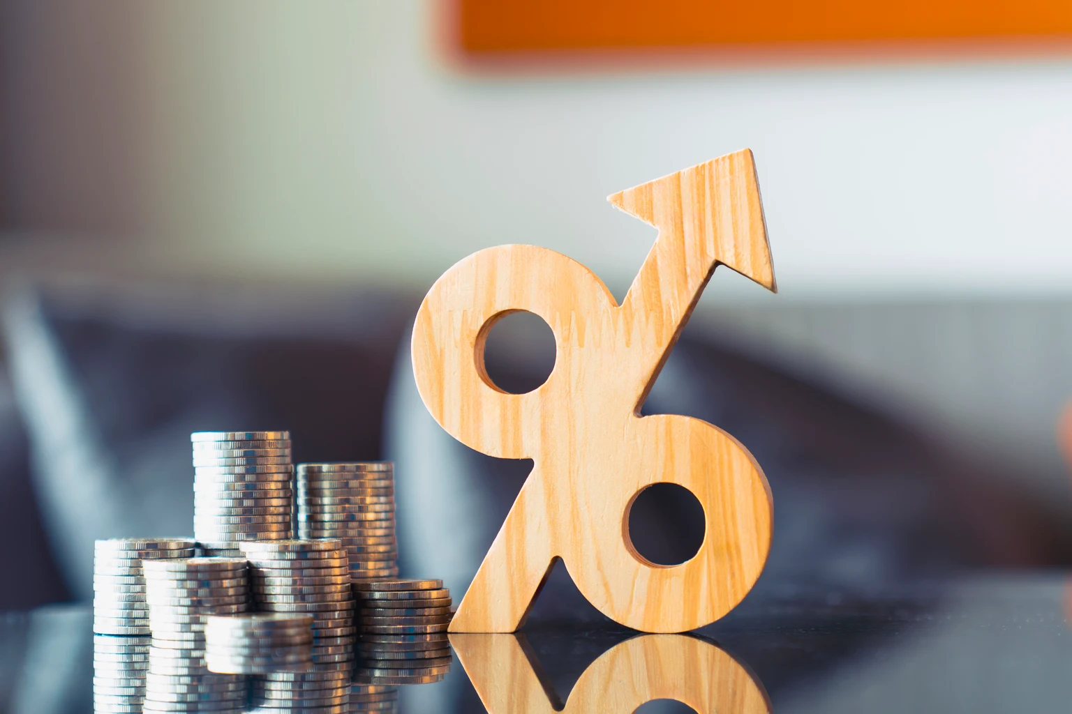 Wooden percentage symbol with upward arrow next to growing coin stacks. Financial interest rate hike, rising inflation, profitable return, and tax growth concept.