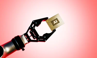 Black robotic arm elevating a golden AI microchip against soft pink gradient background illustrating advanced artificial intelligence hardware and precision robotics engineering