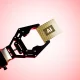 Black robotic arm elevating a golden AI microchip against soft pink gradient background illustrating advanced artificial intelligence hardware and precision robotics engineering