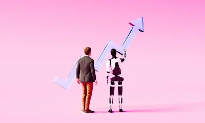Man in suit and humanoid robot viewing blue rising arrow graph together against solid pink background symbolizing collaborative AI-driven business success
