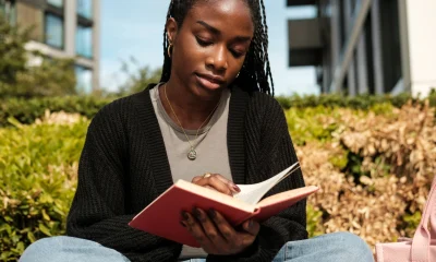 Young black woman reading book outdoors on campus