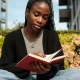 Young black woman reading book outdoors on campus