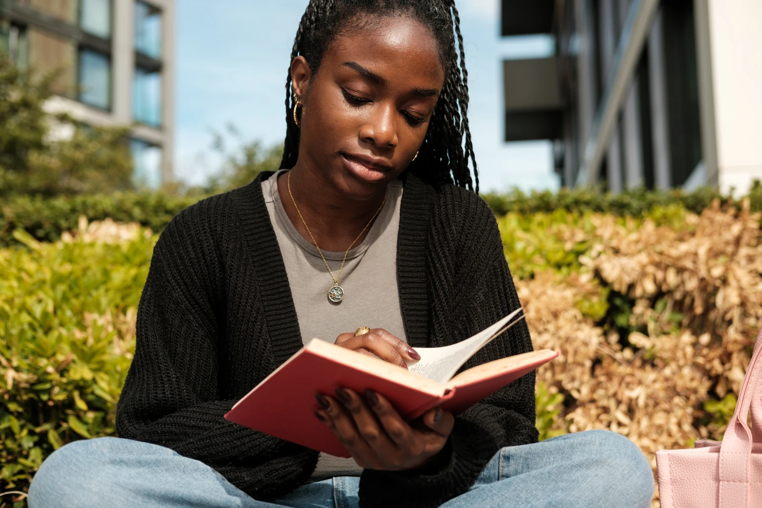 Young black woman reading book outdoors on campus