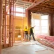 Two construction workers talk together inside large house under renovation