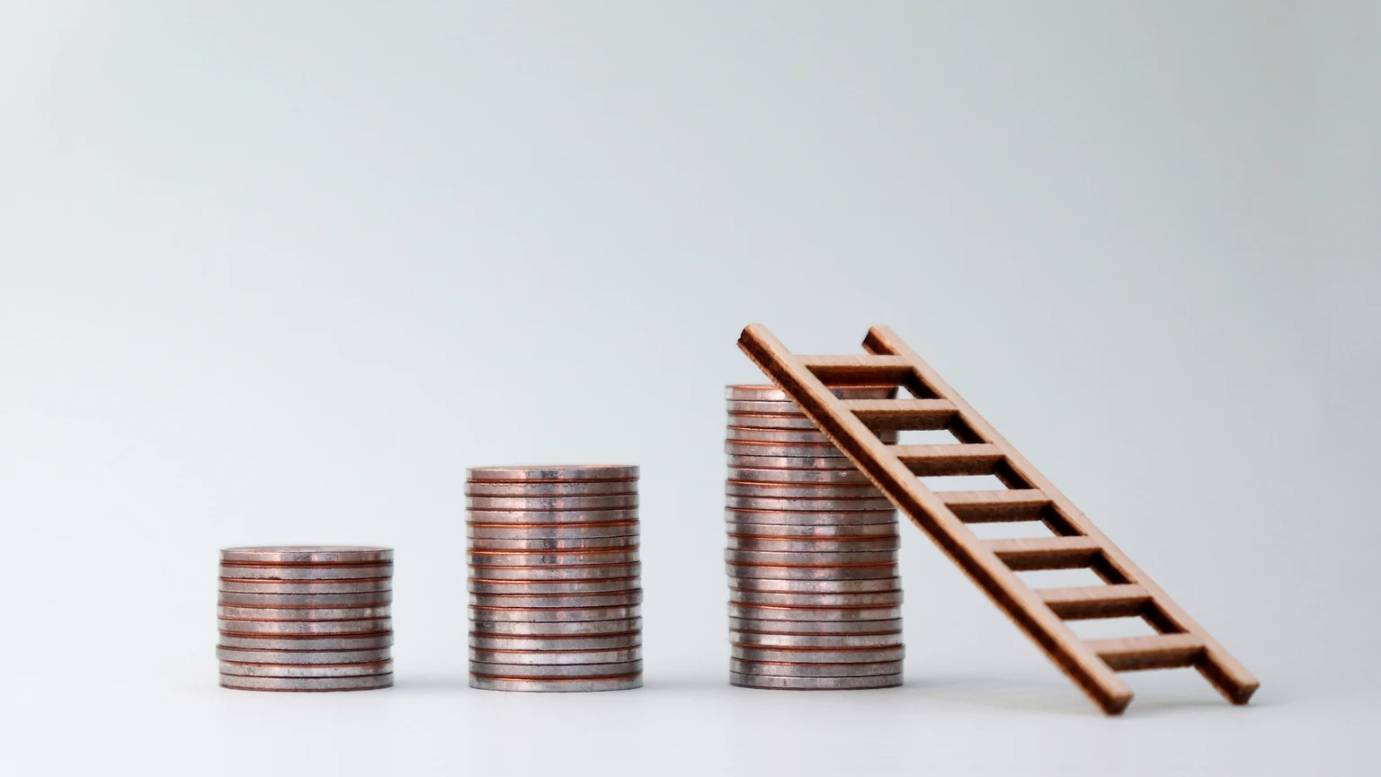 Three pile of coins and a small wooden ladder.