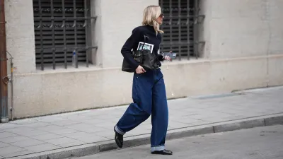 MUNICH, GERMANY - FEBRUARY 18: Mirja Klein is seen wearing a navy fine knit turtleneck sweater with long sleeves and a fitted silhouette from COS; dark wash baggy jeans with a relaxed oversized barrel fit and rolled-up legs from Dark Park; a slim black leather belt with silver buckle; black polished leather loafers with a sleek rounded toe and slim profile from COS; a black „Aventure“ nappa leather bag with gold hardware, chain link details and a belted detail in the front closure from Miu Miu; oversized shield sunglasses with a thick transparent acetate frame and brown tinted lenses from Bottega Veneta; oversized brown shield sunglasses with dark tinted lenses and a thick glossy frame from MM6 Maison Margiela; holding an iPhone smartphone and wearing white wired earphones; her blonde hair is worn long and wavy with a center part on February 18, 2026 in Munich, Germany. (Photo by Moritz Scholz/Getty Images)