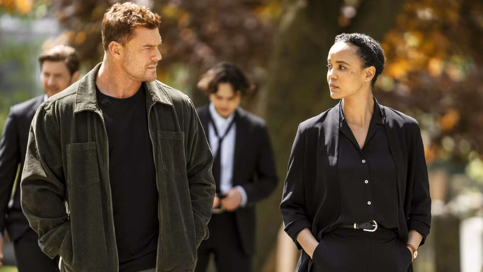 Alan Ritchson as Jack Reacher walking with Maria Sten as Frances Neagley at her father's funeral in Neagley