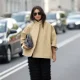 COPENHAGEN, DENMARK - AUGUST 6: Benthe Liem van Esch attending the Munthe show during Copenhagen Fashion Week SS26, is seen wearing a beige cropped cape jacket from Darkpark, called Nat short-sleeve button trench coat, with three-quarter length raglan sleeves, a high collar, single button closure and welt pockets on the front; a pair of lightly transparent wide leg trousers with horizontal tiers of fringes from Munthe, called Laith pants; black open-toe heeled sandals; a white resin bangle bracelet; silver hoop earrings, she is carrying a grey Lixia Bag from Munthe, a handbag in soft leather with top handle; she is wearing aviator sunglasses with metallic golden frame and dark lenses; her straight long brown hair is worn loose during Copenhagen Fashion Week day three on August 6, 2025 in Copenhagen, Denmark. (Photo by Moritz Scholz/Getty Images)