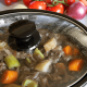 a crockpot slow cooker has the lid on with a beef stew cooking inside; in the background are red tomatoes and a blue and green kitchen towel