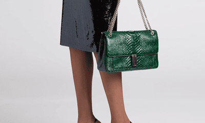 Black woman holds an emerald green bag; she is wearing a sparkly skirt and Very High Heels