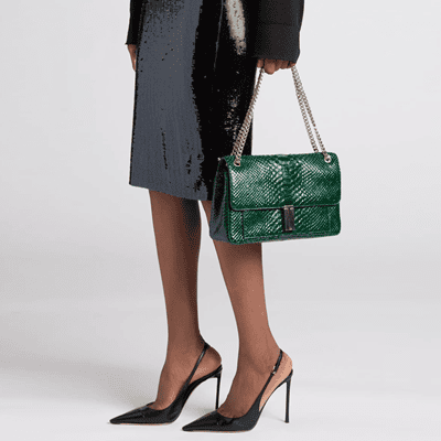 Black woman holds an emerald green bag; she is wearing a sparkly skirt and Very High Heels