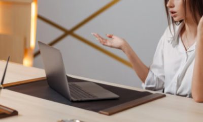 Woman sighs in exasperation at something on her laptop; she has taken off her eyeglasses and holds one hand out in a WTF gesture
