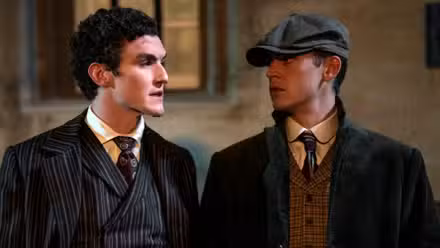 Hero Fiennes Tiffin as Sherlock and Dónal Finn as Moriarty standing next to each other in Young Sherlock