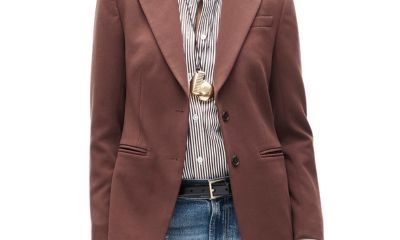 a woman wearing a brown blazer, pinstriped shirt, two necklaces, black belt, an blue jeans