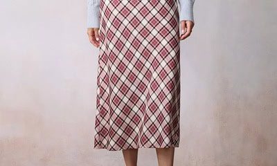 A woman wearing a red plaid midi skirt, black mules, and a light blue sweater