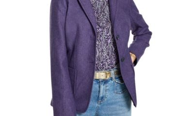 A woman wearing blue jeans, a purple print top, purple blazer, and gold belt